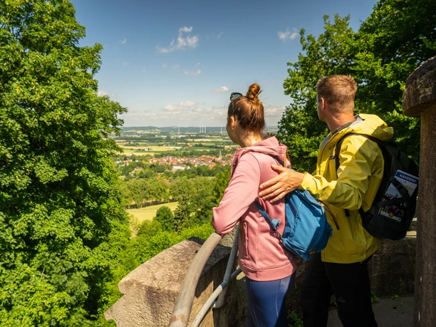 Teutoburger-Wald-Stadt-Nieheim-D-Ketz-127.jpg Zwei Menschen mit Rucksäcken blicken von einer Aussichtsplattform auf Nieheim und die Landschaft.