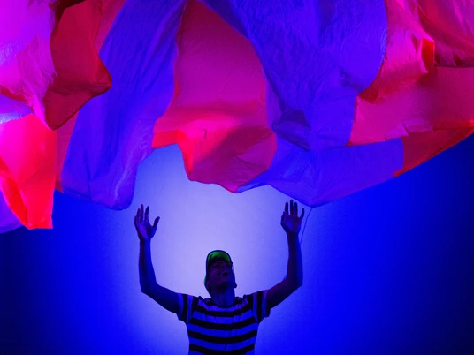 LUNARIS - Ein Weltraummärchen.jpg Das Bild zeigt einen Menschen in einem gestreiften Oberteil, der ein ebenso gestreiftes großes Tuch in den Himmel wirft.