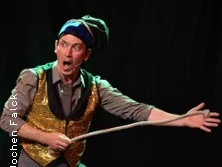 Ein Mann in bunter Kleidung, gestikulierend auf einer Bühne.