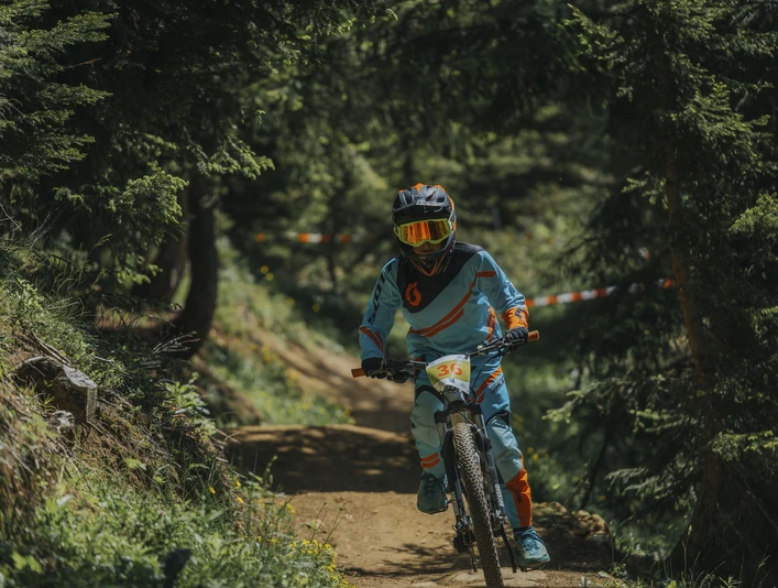 Kind im Bike-Rennen auf dem Flowtrail Kinderbikekurs Riederalp mit jungem Biker im Schutzanzug auf dem Flowtrail der Aletsch ArenaChildren's bike course Riederalp with a young biker in a protective suit on the Aletsch Arena flow trailCours de VTT pour enfants à Riederalp avec un jeune vététiste en combinaison de protection sur le flowtrail de l'Aletsch Arena