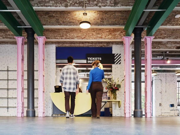 Schirn Dondorf Druckerei Foyer mit Tickets/Info, rosa Säulen, zwei Besucher*innen im Vorbeigehen