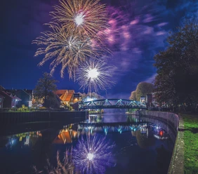 Farbenprächtiges Feuerwerk über einer Brücke in Meppen mit Spiegelung im Wasser bei Nacht