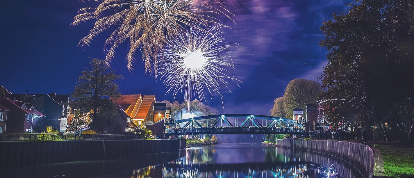 Farbenprächtiges Feuerwerk über einer Brücke in Meppen mit Spiegelung im Wasser bei Nacht