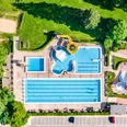Luftaufnahme eines Freibads in Bad Driburg mit Schwimmbecken, gelber Rutsche und Grünflächen