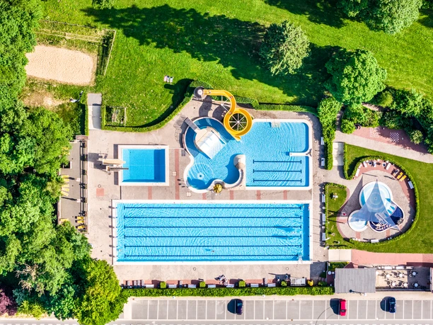 Luftaufnahme eines Freibads in Bad Driburg mit Schwimmbecken, gelber Rutsche und Grünflächen