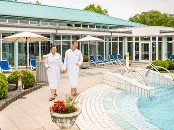 Bad-Driburg-Driburg-Therme-Außenbecken-Teutoburger-Wald-Bad-Driburger-Touristik-GmbH-D-Ketz-127-CC-BY-SA.jpg Ein Paar im Bademantel geht am Außenbecken der Driburg-Therme entlang, umgeben von Liegen und Sonnenschirmen.