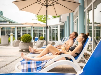 Bad-Driburg-Driburg-Therme-Außenbecken-Teutoburger-Wald-Bad-Driburger-Touristik-GmbH-D-Ketz-143.jpg Zwei Personen auf Liegestühlen unter Sonnenschirmen vor der Driburg Therme in Bad Driburg.