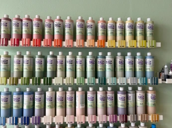 Lieblingstasse-Farben.jpg Farbflaschen nach Farben geordnet in Reihe an einer Wand