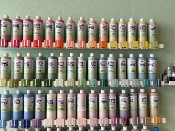 Lieblingstasse-Farben.jpg Farbflaschen nach Farben geordnet in Reihe an einer Wand