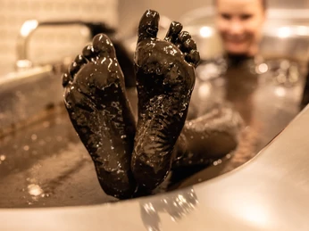 Bad-Driburg-Graefliches-Gesundheitszentrum-Moorbad-Teutoburger-Wald-Bad-Driburger-Touristik-GmbH-D-Ketz-176.jpg Person entspannt im Moorbad, beide schwarz gefärbten Füße ragen aus dem warmen Wasser hervor.