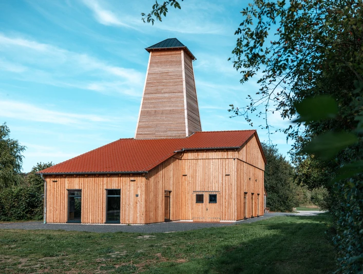 Saline Salzderhelden ©Florian Spieker Holzverkleidetes Saline mit rotem Satteldach und hohem Turm, umgeben von Bäumen und Wiese.