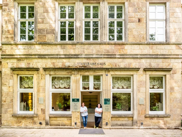 Bad-Driburg-Graefliches-Gesundheitszentrum-Teutoburger-Wald-Bad-Driburger-Touristik-GmbH-D-Ketz-198.jpg Historisches Gebäude aus Sandstein mit Aufschrift Stahlbadehaus, zwei Personen am Eingangsportal.