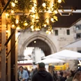 After-work market on Chlodwigplatz Ein belebter Marktplatz bei Dämmerung, mit Lichterketten und einem historischen Torbogen im Hintergrund.A lively market square at dusk, with fairy lights and a historic archway in the background.