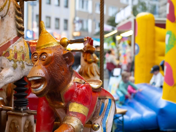Carousel, Feierabendmarkt auf dem Chlodwigplatz A colorful carousel with a monkey as a motif and a shining roof on a city square.