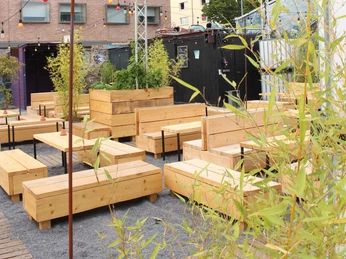 Der schwarze Hase Holzbänke auf einem modernen Außenbereich mit urbanem Ambiente und umgebenden Pflanzen.Wooden benches in a modern outdoor area with an urban ambience and surrounding plants.