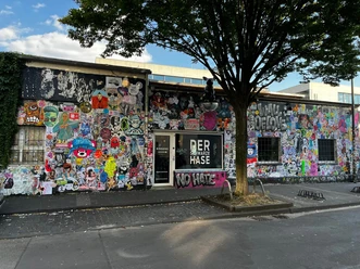 Der schwarze Hase Graffiti-bedeckte Fassade eines Gebäudes in urbaner Umgebung mit teils farbenfrohen Motiven.