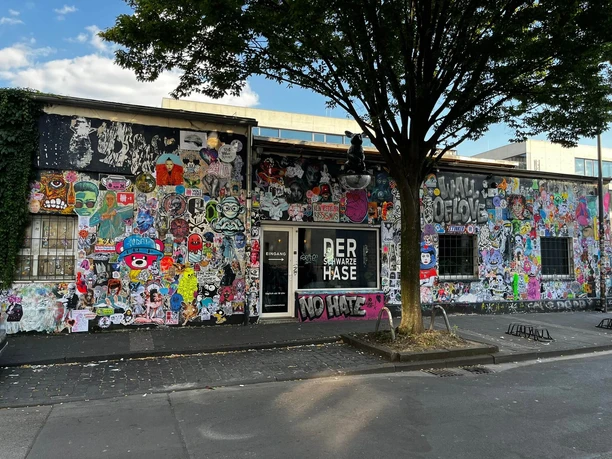 Der schwarze Hase Graffiti-bedeckte Fassade eines Gebäudes in urbaner Umgebung mit teils farbenfrohen Motiven.