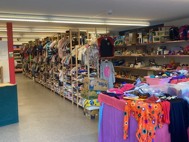 Offre de la bourse aux vêtements d'enfants Simme Salle d'exposition d'une bourse aux vêtements pour enfants, avec des vêtements pour enfants, des jouets et des accessoires pour enfants présentés sur des étagères et des tables de vente.
