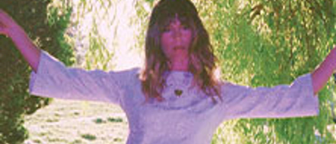 Frau in weißem Kleid unter einem Baum, umgeben von grünem Laub bei Sonnenschein.