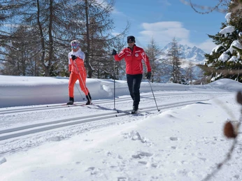 Cross-country skiing course on the groomed trail of the Riederalp Langlauf Schnupperkurs Riederalp mit zwei Teilnehmern auf gespurter Loipe vor verschneiter AlpenkulisseCross-country skiing taster course Riederalp with two participants on a groomed trail against a snowy Alpine backdropCours d'initiation au ski de fond à Riederalp avec deux participants sur une piste tracée devant un décor alpin enneigé