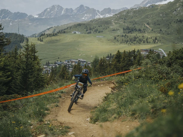 Child at the bike race on the Bettmeralp Bettmeralp children's bike course with a young participant on the flow trail against the mountain backdrop of the Aletsch Arena