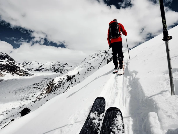 Skitour oberhalb des Aletschgletschers Aletschgletscher Rundtour Ski mit Skitourengeher auf verschneitem Grat oberhalb des Gletschers, Aufstieg bei Wolken und Sonne