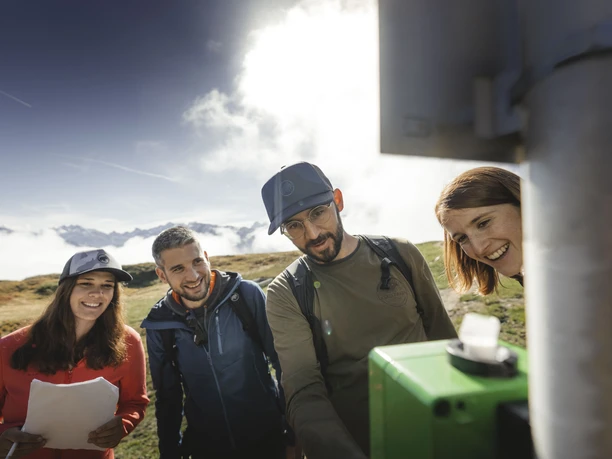 Esprit d'équipe au Foxtrail Desoria Foxtrail Desoria Aletsch Arena avec quatre participants qui résolvent ensemble une tâche sur une boîte verte