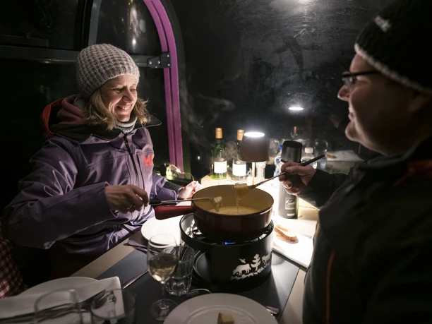 Enjoyable fondue experience in winter Bettmerhorn fondue gondola with couple enjoying a cheese fondue in an atmospheric gondola in the snowy Aletsch Arena in the evening