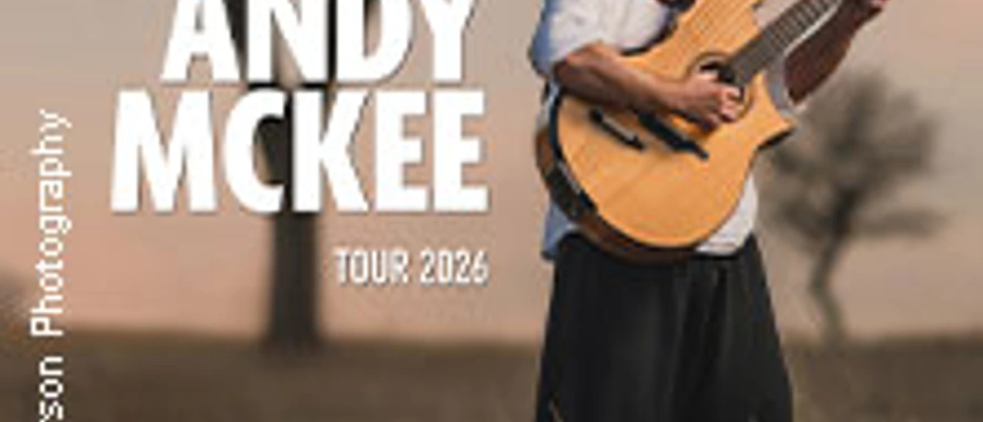 Der Musiker Andy McKee steht mit zwei Gitarren auf einem Feld bei Sonnenuntergang.