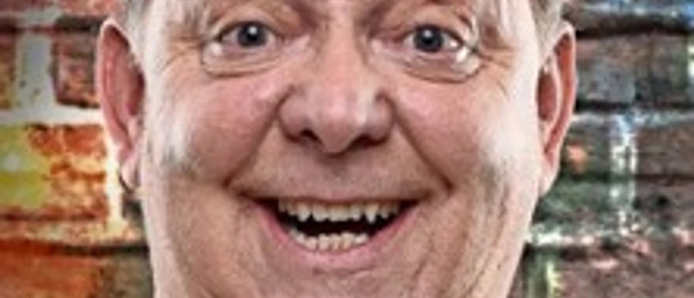 Fröhlich lächelnder Mann vor bunter Ziegelmauer.