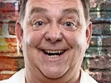 Fröhlich lächelnder Mann vor bunter Ziegelmauer.