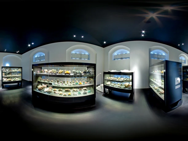 terra_mineralia_afrika_druck.jpg Eine Ausstellungshalle mit beleuchteten Glasvitrinen voller verschiedener Mineralien und Gesteine.