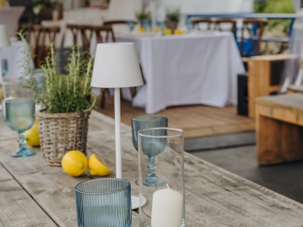Eine rustikale Holztafel mit blauen Gläsern, Zitronen und Kerzen unter einem Zelt.
