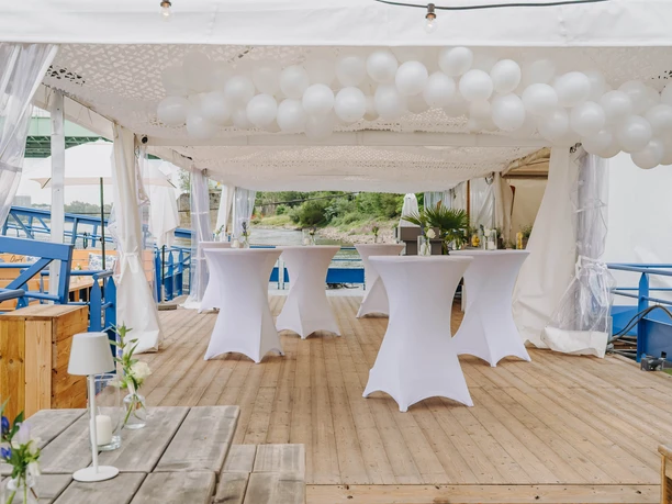 IMG_4664.JPG Weiße Stehtische und runde Ballons unter Pavillon auf Holzdeck mit Seeblick.