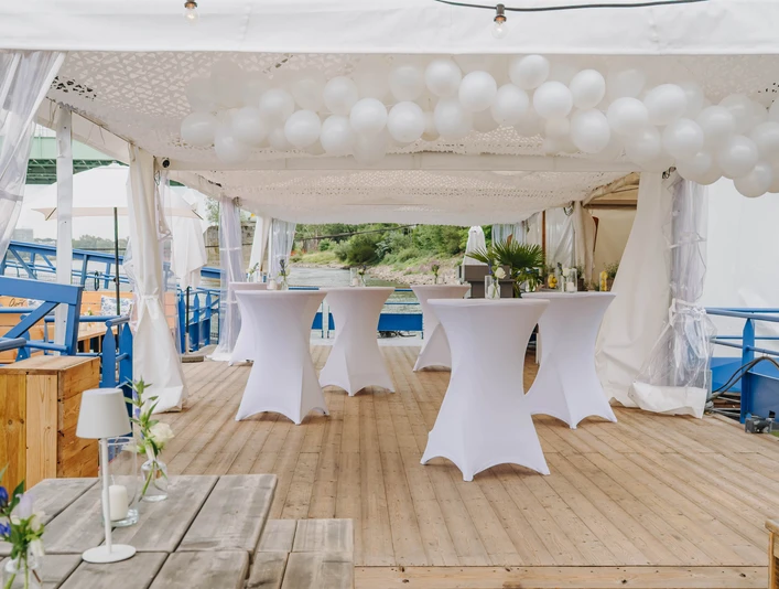 IMG_4664.JPG Weiße Stehtische und runde Ballons unter Pavillon auf Holzdeck mit Seeblick.White bar tables and round balloons under a pavilion on a wooden deck with a view of the lake.