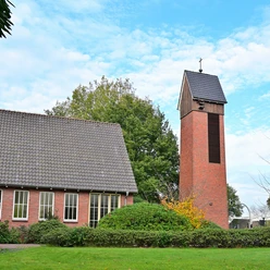 Die Friedenskirche Augustfehn ist ein eindrucksvoller roter Backsteinturm, umgeben von grünen Büschen und Bäumen