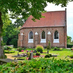 Die Kapelle in Vreschen-Bokel aus Backstein mit roten Dachziegeln, umgeben von gepflegten Gräbern und Pflanzen.