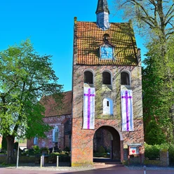 Ansicht des charmanten Backstein-Glockenturms von St. Nikolai in Apen, eingerahmt von grünen Bäumen