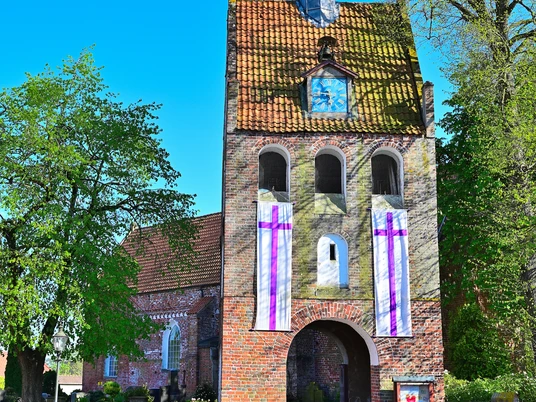 St. Nikolai Kirche Ansicht des charmanten Backstein-Glockenturms von St. Nikolai in Apen, eingerahmt von grünen Bäumen