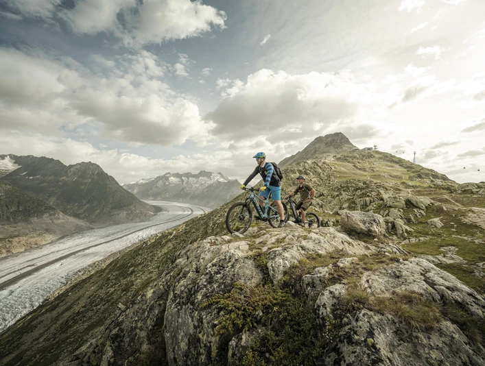 Mountain biking with a glacier view Aletsch Bikepass mit Bikern auf dem Trail oberhalb des Grossen Aletschgletschers mit weiter Aussicht über die Aletsch ArenaAletsch Bikepass with bikers on the trail above the Great Aletsch Glacier with sweeping views over the Aletsch ArenaAletsch Bikepass avec des vététistes sur le trail au-dessus du grand glacier d'Aletsch avec une large vue sur l'Aletsch Arena