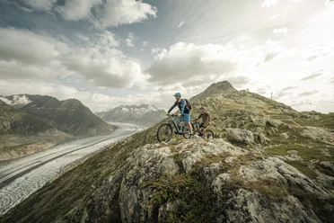 VTT avec vue sur le glacier Aletsch Bikepass avec des vététistes sur le trail au-dessus du grand glacier d'Aletsch avec une large vue sur l'Aletsch Arena