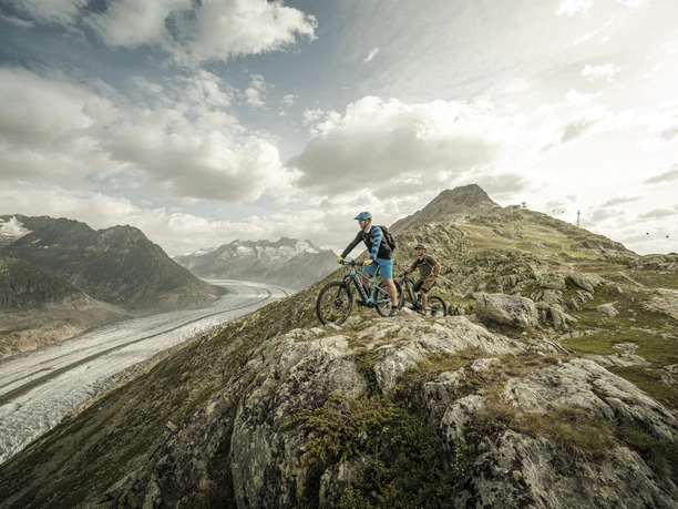 VTT avec vue sur le glacier Aletsch Bikepass avec des vététistes sur le trail au-dessus du grand glacier d'Aletsch avec une large vue sur l'Aletsch Arena