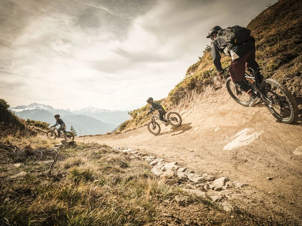 Flowtrail Wurzenbord Bettmeralp Aletsch Bikepass avec des vététistes sur le flowtrail Wurzenbord lors d'une descente rapide avec vue sur les Alpes valaisannes