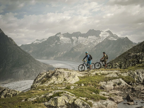 Faire du vélo avec vue sur le glacier d'Aletsch Bike Genuss Tour Aletsch Arena avec des vététistes au-dessus du grand glacier d'Aletsch sur un parcours panoramique savoureux en Valais
