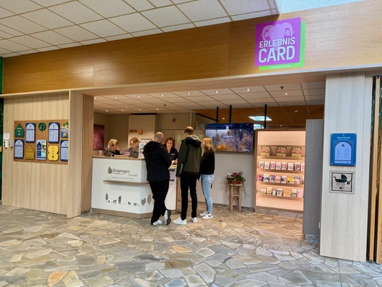 Bispingen-Touristik-Center-Parcs.jpg Empfangsbereich der Bispingen Touristik im Center Parcs mit Informationsschalter, Personal und Besuchern.