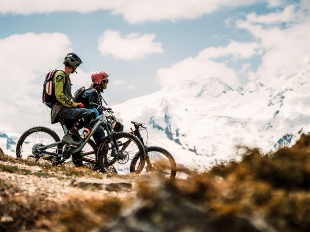 Biking against a snowy Alpine backdrop Upper Valais bike pass with bikers on an alpine trail with views of the snow-capped peaks of the Valais Alps in Saas Fee