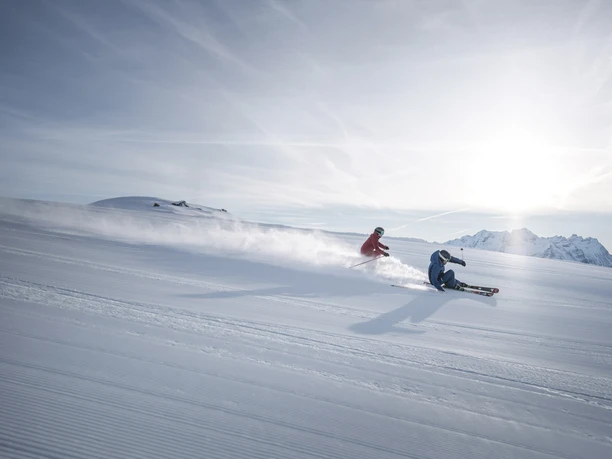 Des virages parfaits sur des pistes fraîches Forfait Aletsch Arena avec deux skieurs en train de faire du carving sportif sur une piste parfaitement préparée sous le soleil d'hiver