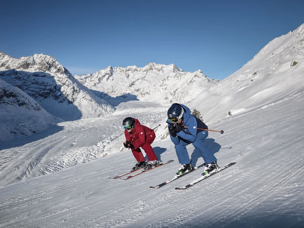 Skifahren mit Blick auf den Aletschgletscher Skipass Aletsch Arena mit zwei Skifahrern auf perfekt präparierter Piste oberhalb des Aletschgletschers bei strahlendem Winterwetter