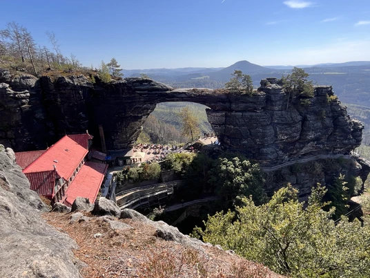Aussicht Prebischtor Im Vordergrund ein Dach der Gaststätte im Hintergrund aus Sandsteinfelsen ein großes Felsentor