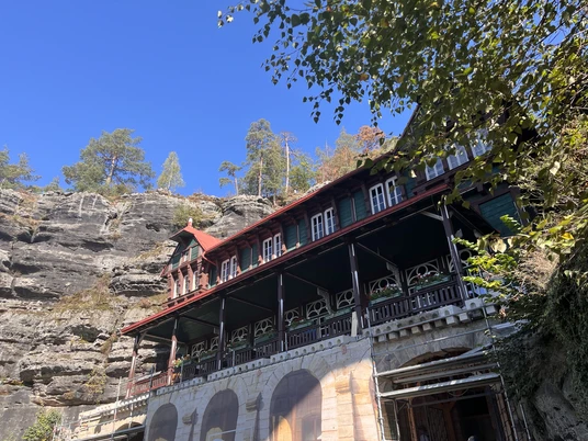 Gaststätte Falkennest am Prebischtor Vordergrund Gaststätte im Schweizer Baustil und im Hintergrund Sandsteinfelsen.